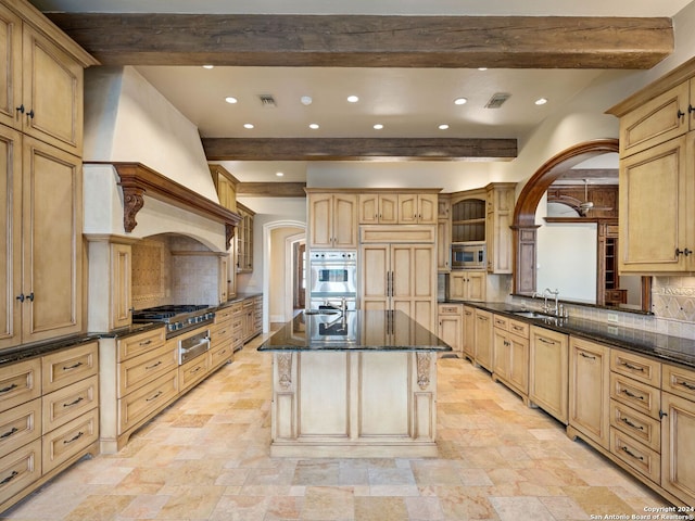 kitchen with tasteful backsplash, beamed ceiling, built in appliances, a kitchen island with sink, and light brown cabinetry