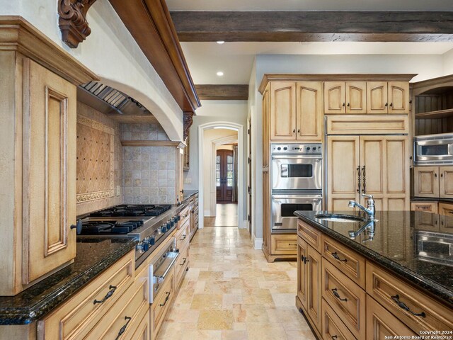 kitchen with built in appliances, decorative backsplash, dark stone countertops, and sink