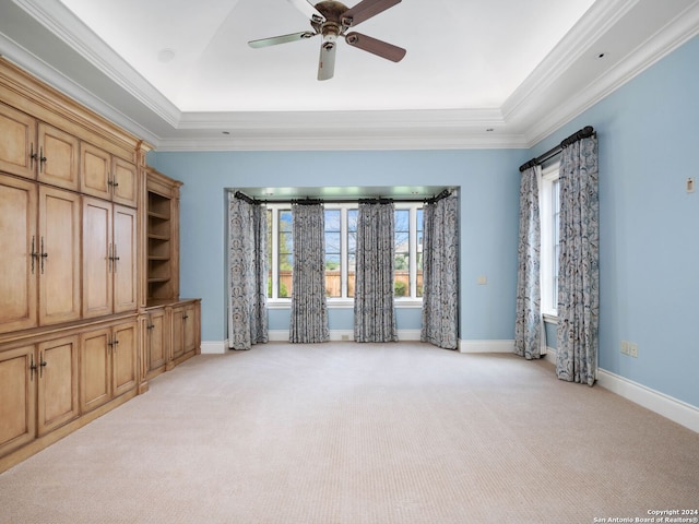 unfurnished living room with a tray ceiling, ceiling fan, crown molding, and light colored carpet