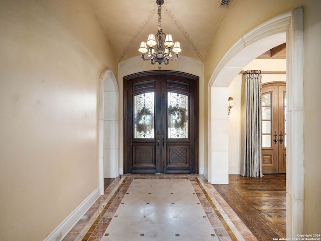 foyer entrance featuring a notable chandelier, french doors, vaulted ceiling, and hardwood / wood-style flooring