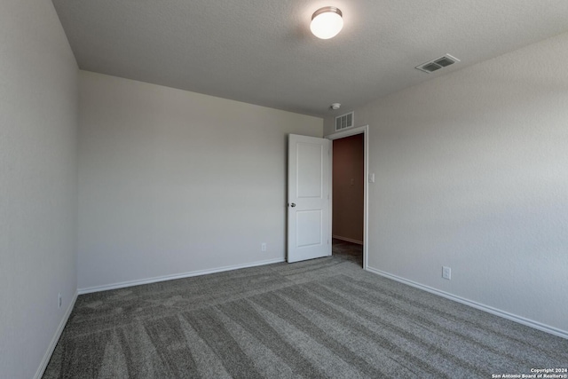 empty room featuring a textured ceiling and dark colored carpet