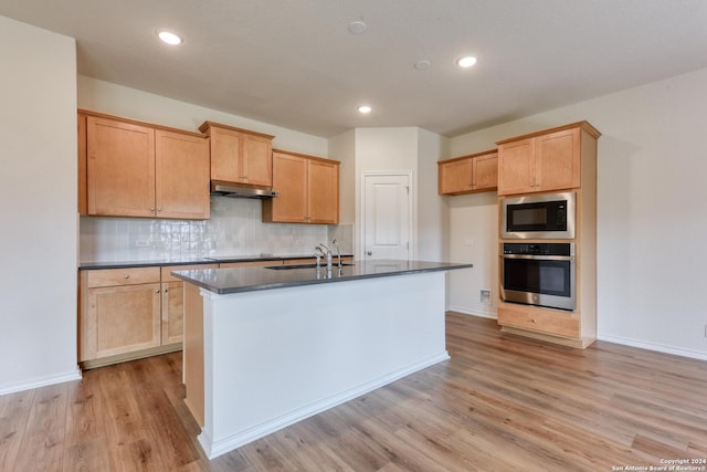 kitchen featuring stainless steel oven, a center island with sink, sink, light hardwood / wood-style flooring, and built in microwave