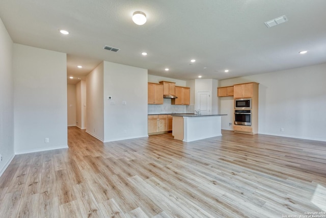 kitchen with built in microwave, light hardwood / wood-style flooring, oven, an island with sink, and decorative backsplash