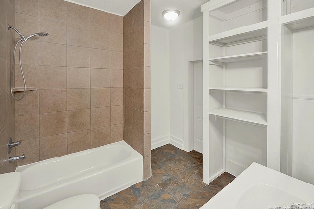 bathroom with toilet, a textured ceiling, and tiled shower / bath