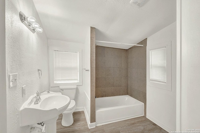 bathroom with tiled shower / bath combo, a textured ceiling, vaulted ceiling, wood-type flooring, and toilet