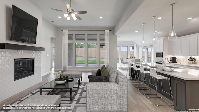 living room featuring a brick fireplace, ceiling fan, sink, and light hardwood / wood-style flooring