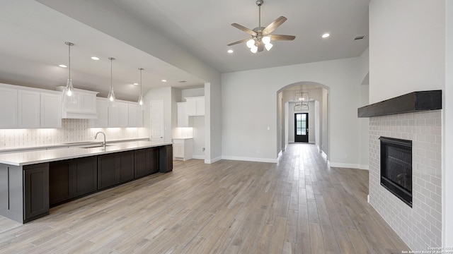 kitchen featuring ceiling fan, tasteful backsplash, light hardwood / wood-style flooring, a center island with sink, and white cabinets