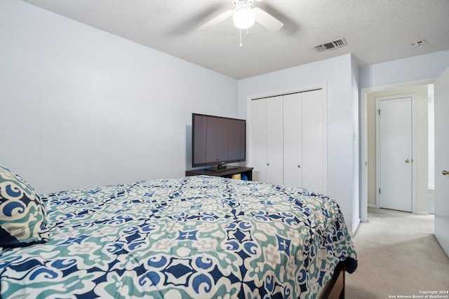 bedroom with ceiling fan, a closet, light carpet, and a textured ceiling