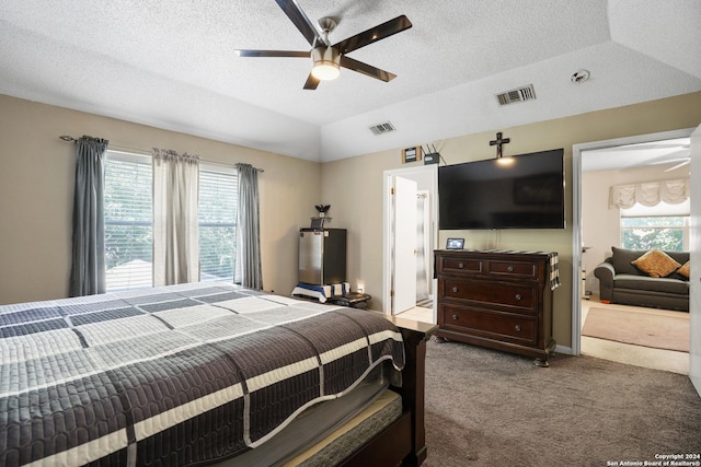 bedroom with carpet flooring, a textured ceiling, vaulted ceiling, ceiling fan, and connected bathroom