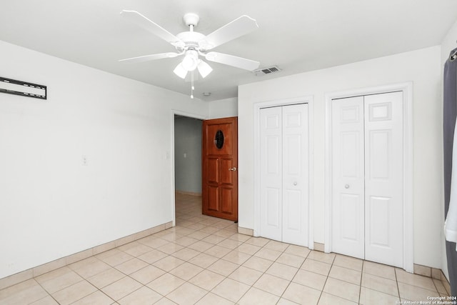 unfurnished bedroom featuring light tile patterned floors, ceiling fan, visible vents, and multiple closets