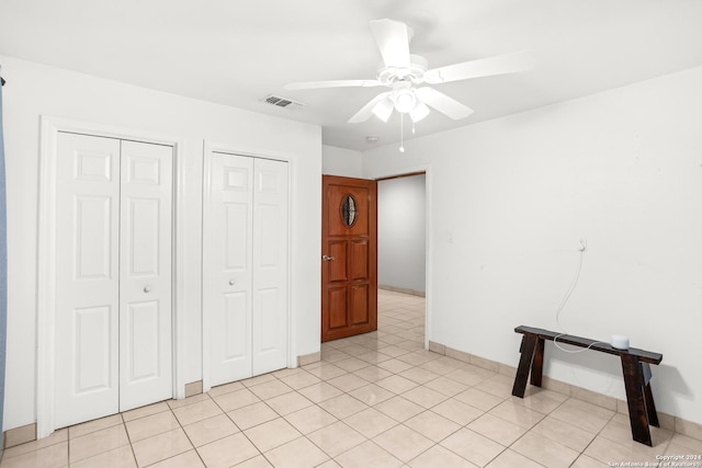 unfurnished bedroom with light tile patterned floors, ceiling fan, visible vents, and two closets