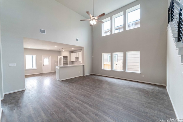 unfurnished living room with ceiling fan, dark hardwood / wood-style floors, and a high ceiling