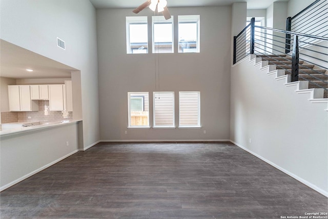 unfurnished living room featuring ceiling fan, plenty of natural light, a towering ceiling, and dark hardwood / wood-style floors