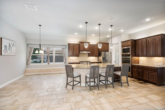 kitchen featuring appliances with stainless steel finishes, pendant lighting, light stone countertops, dark brown cabinets, and a spacious island