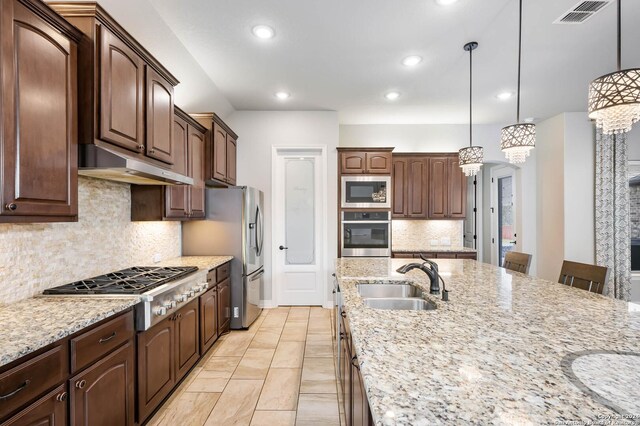 kitchen with appliances with stainless steel finishes, pendant lighting, sink, tasteful backsplash, and a kitchen bar