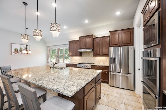 kitchen featuring decorative light fixtures, backsplash, an island with sink, appliances with stainless steel finishes, and sink