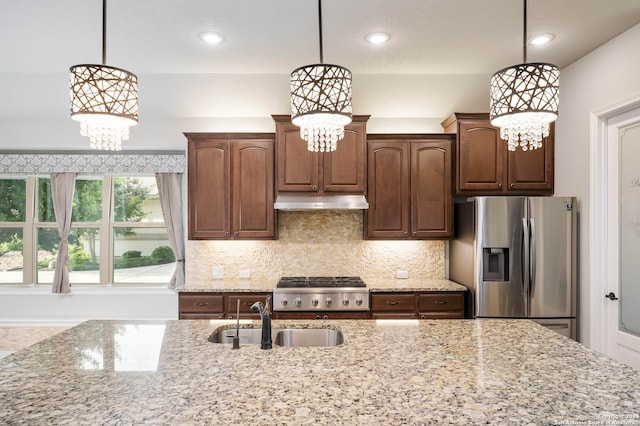 kitchen with appliances with stainless steel finishes, a chandelier, light stone counters, and decorative light fixtures