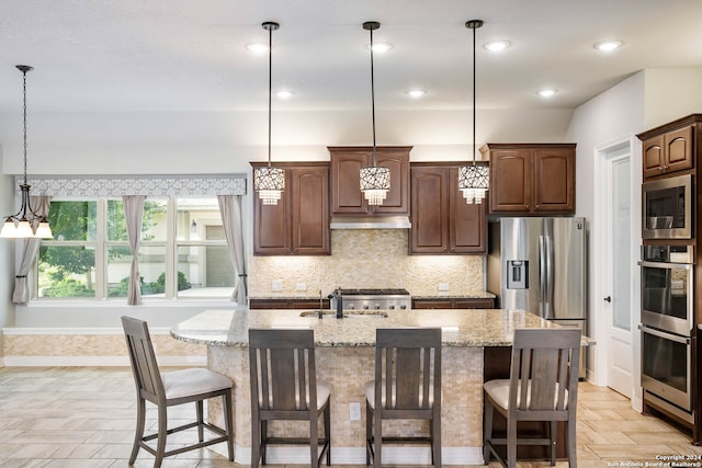 kitchen featuring stainless steel appliances, a center island with sink, tasteful backsplash, and pendant lighting