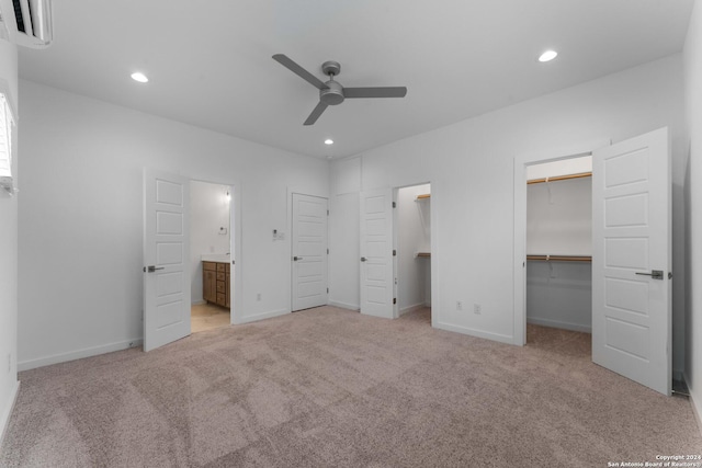 unfurnished bedroom with a spacious closet, ensuite bath, a closet, light colored carpet, and ceiling fan