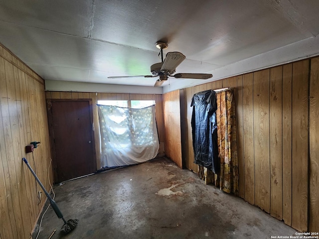 unfurnished room featuring ceiling fan, concrete flooring, and wooden walls