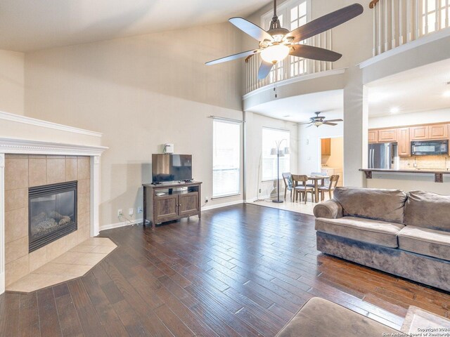 living room featuring dark hardwood / wood-style floors, high vaulted ceiling, ceiling fan, and a tiled fireplace