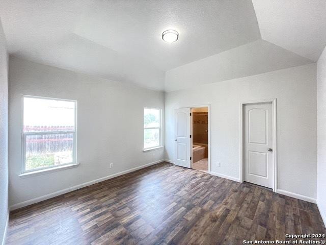 unfurnished bedroom featuring ensuite bathroom, dark hardwood / wood-style flooring, a textured ceiling, and vaulted ceiling