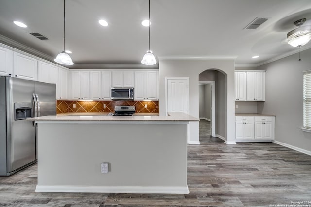 kitchen featuring appliances with stainless steel finishes, decorative light fixtures, white cabinetry, a kitchen island with sink, and crown molding