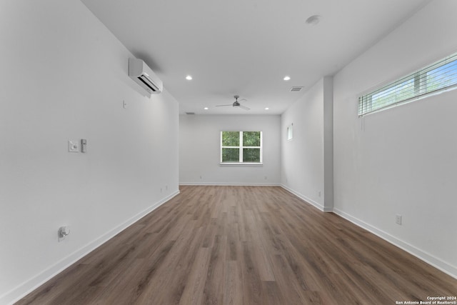 spare room featuring hardwood / wood-style flooring, a wall unit AC, and ceiling fan