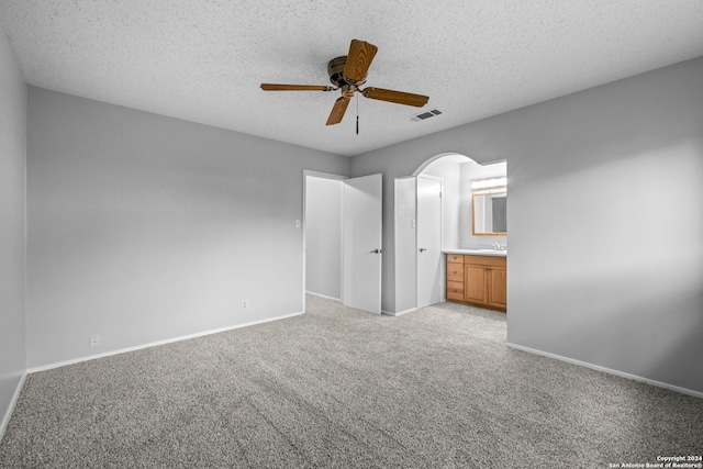 unfurnished bedroom with ensuite bath, ceiling fan, light colored carpet, and a textured ceiling