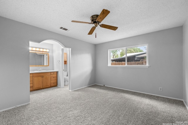 unfurnished bedroom with ceiling fan, a textured ceiling, light carpet, and ensuite bath