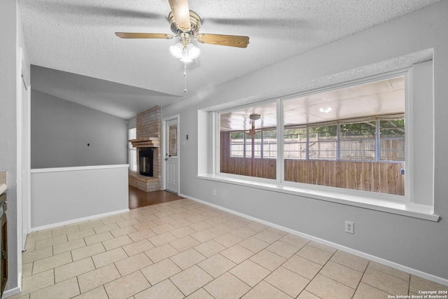 tiled empty room with ceiling fan, lofted ceiling, a textured ceiling, and a brick fireplace