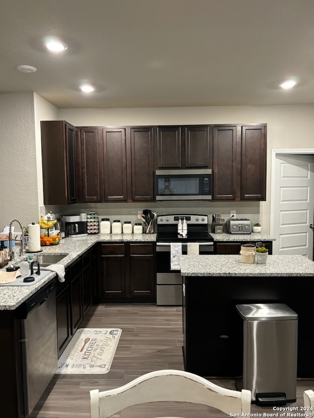 kitchen featuring stainless steel appliances, light wood-type flooring, sink, light stone counters, and dark brown cabinetry