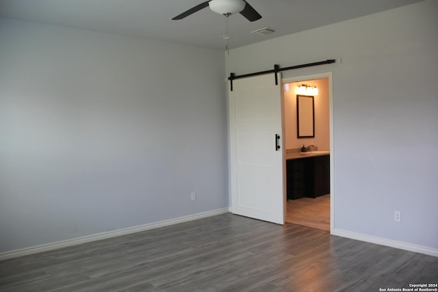 spare room with ceiling fan, a barn door, and dark wood-type flooring