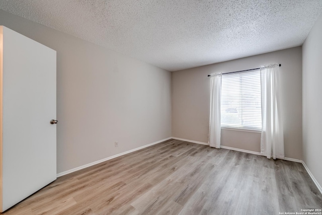 spare room with a textured ceiling and light hardwood / wood-style flooring