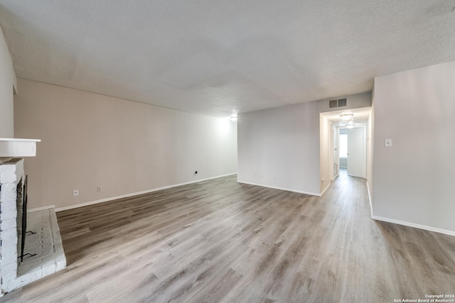 unfurnished living room featuring a brick fireplace, a textured ceiling, and light wood-type flooring