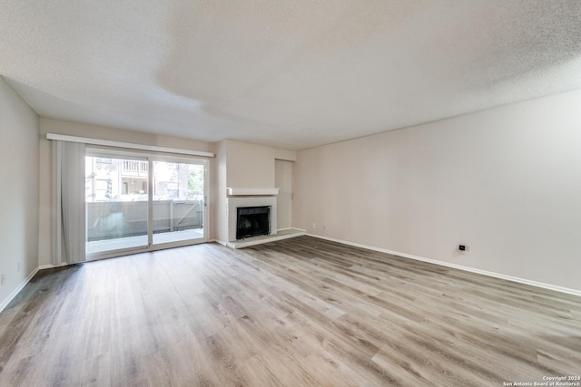 unfurnished living room featuring a brick fireplace, light hardwood / wood-style floors, and a textured ceiling