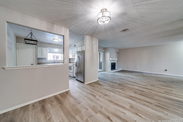 unfurnished living room featuring sink, a textured ceiling, and light hardwood / wood-style floors