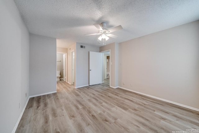 unfurnished bedroom with a textured ceiling, ceiling fan, ensuite bathroom, and light hardwood / wood-style flooring