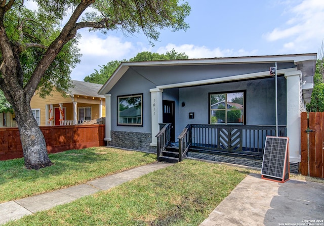 bungalow-style home with covered porch, a front yard, fence, and stucco siding