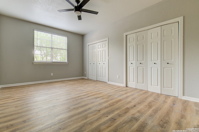 unfurnished bedroom with ceiling fan, multiple closets, and wood-type flooring