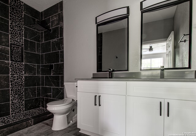 bathroom with tiled shower, tile flooring, ceiling fan, vanity, and toilet