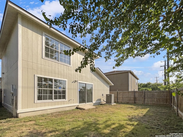 rear view of house with central air condition unit and a lawn