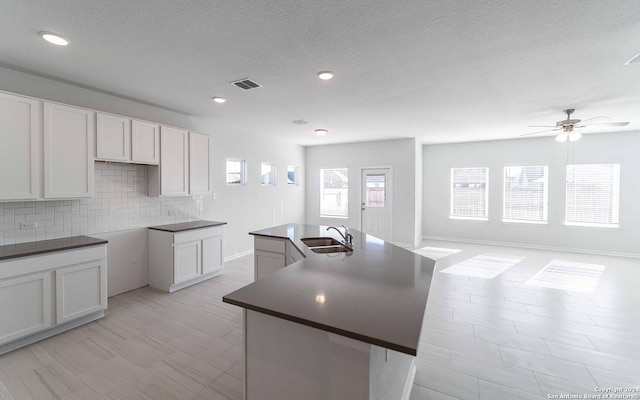 kitchen with dark countertops, a center island with sink, white cabinets, and a sink