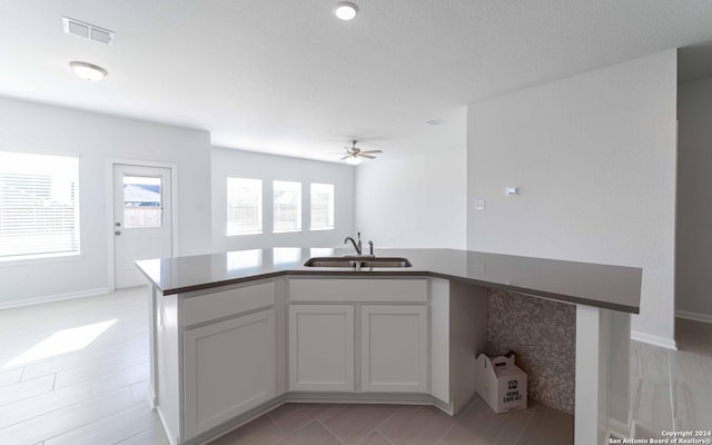 kitchen with visible vents, a ceiling fan, open floor plan, white cabinetry, and a sink