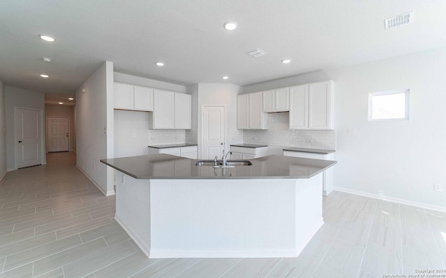 kitchen featuring tasteful backsplash, visible vents, white cabinets, a kitchen island with sink, and a sink