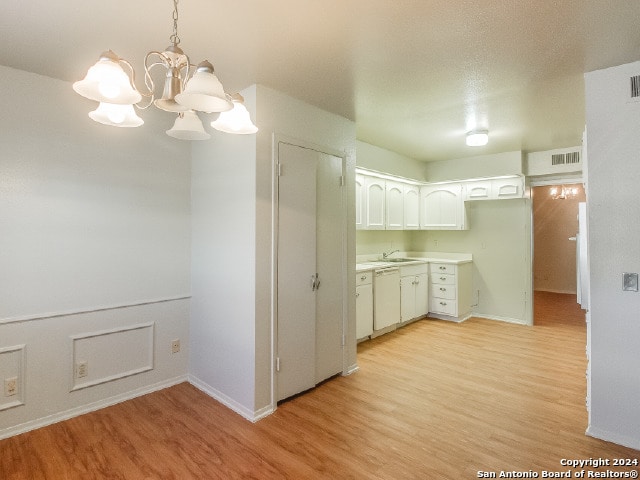 kitchen with light wood-type flooring, white dishwasher, decorative light fixtures, a notable chandelier, and white cabinetry