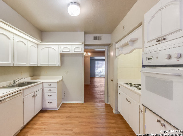 kitchen with white appliances, white cabinets, sink, light hardwood / wood-style floors, and a chandelier