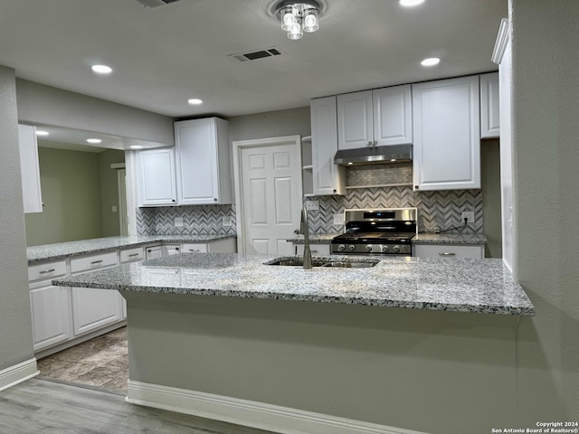 kitchen featuring white cabinets, sink, stainless steel gas stove, light stone countertops, and kitchen peninsula