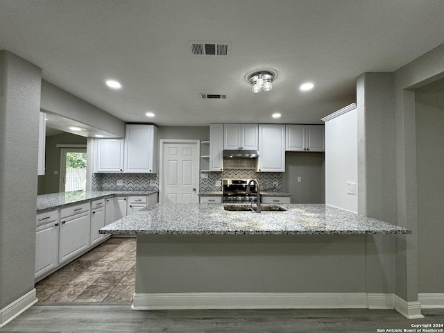 kitchen featuring white cabinets, light stone countertops, kitchen peninsula, and sink