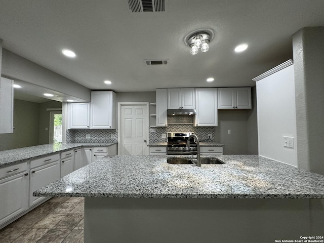 kitchen featuring sink, decorative backsplash, light stone countertops, stainless steel range oven, and white cabinetry